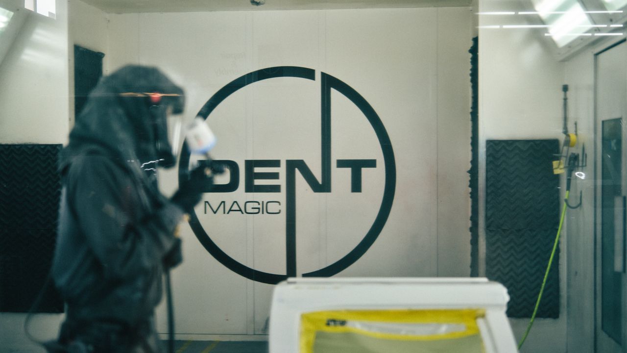 Dent Magic painter in the spray booth at the logo wall